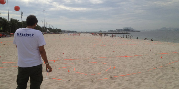 Beach with orange flags connected with orange tape set in the sand, guy in a tcktcktck T-shirt assessing it