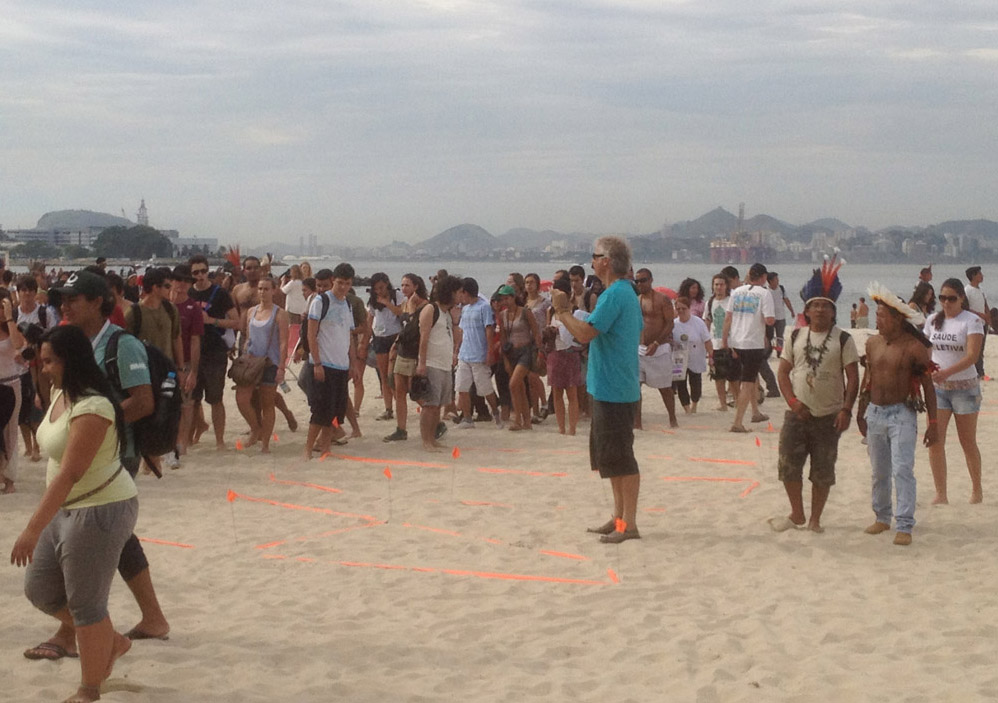 John in the middle of a big circle of people standing on the beach